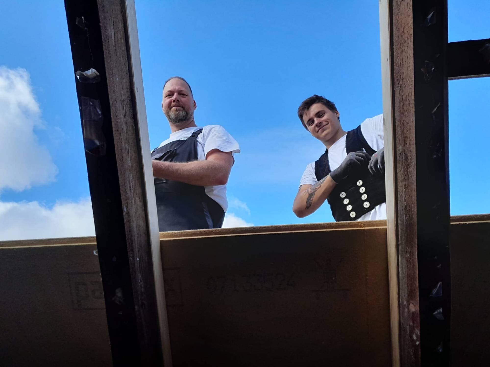 Die Mitarbeiter Dennis und Paul schauen bei Dacharbeiten durch die Sparren nach unten